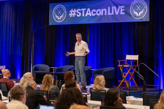 Speaker on the STACon Live mainstage with attendees seated in front.