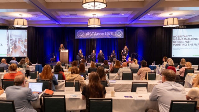 Panel discussion on the STACon Live stage with five panelists seated.