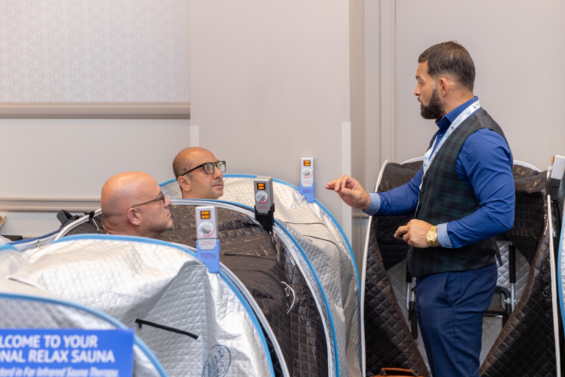 Two attendees inside Relax Sauna pods being walked through controls.