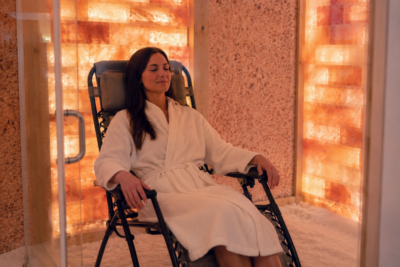Guest relaxing in a robe inside a warmly lit Himalayan salt room.