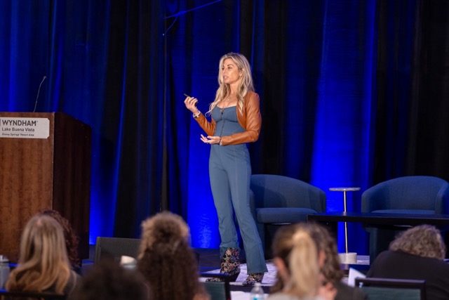 Speaker presenting on the STACon stage in a blue jumpsuit.