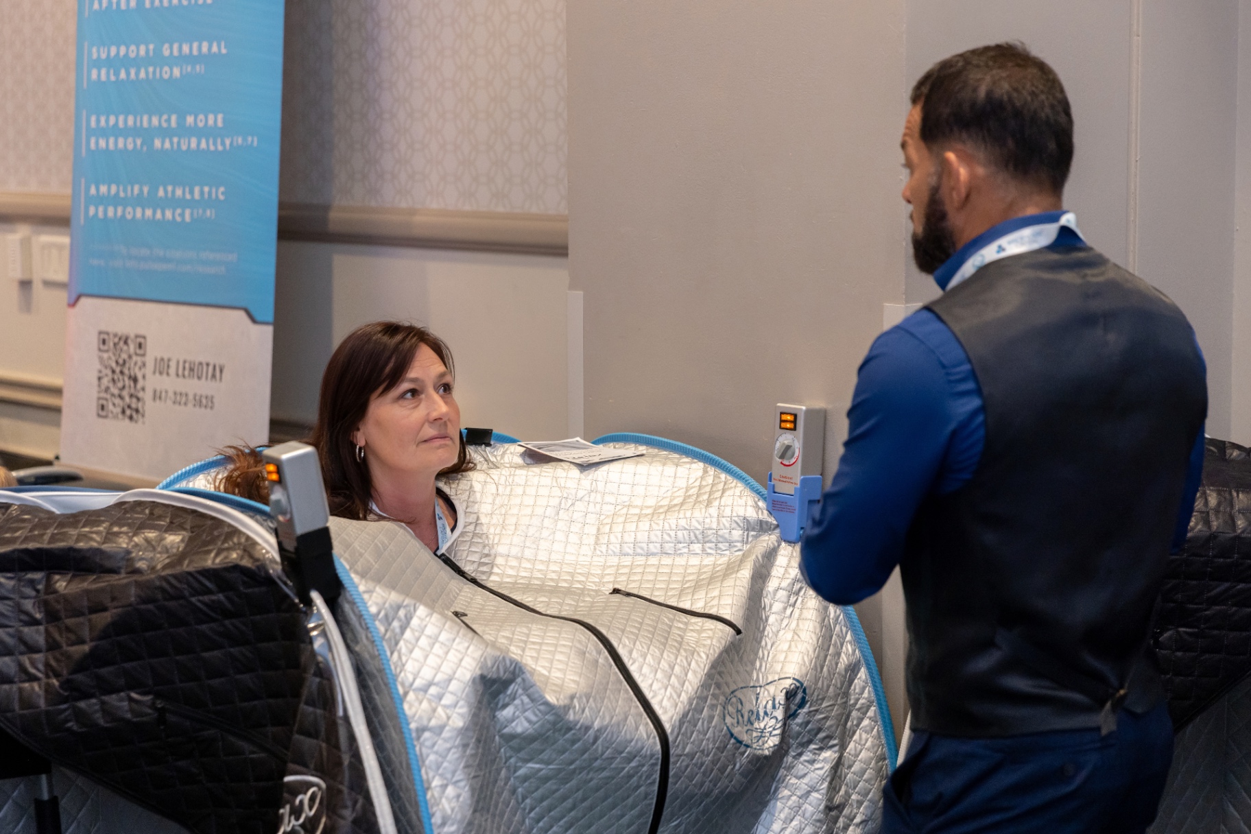 Vendor demonstrating an infrared Relax Sauna to a seated attendee.