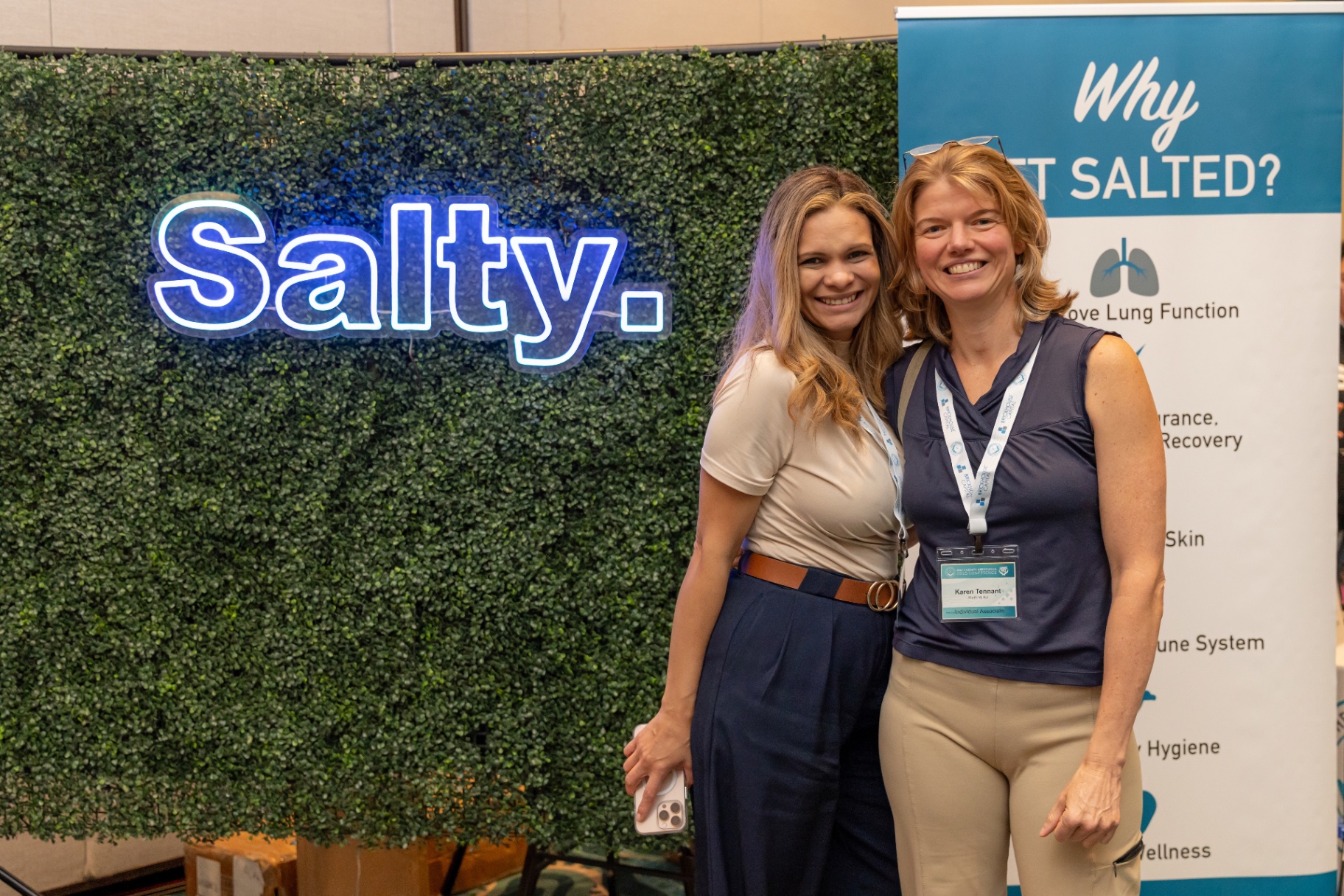 Two attendees smiling in front of the Salty neon sign at STACon.